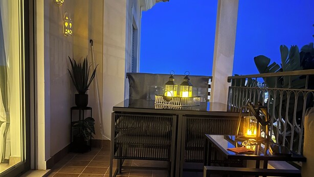 Ein Balkon mit Tisch, Stühlen, Topfpflanzen und dekorativer Beleuchtung.