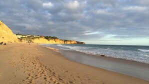 Ein sandiger Strand mit Fußabdrücken, eine bewachsene Klippe und das Meer.