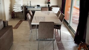 Un coin repas avec une table et des chaises, un canapé, une statuette de tigre décorative et une grande fenêtre avec des rideaux.