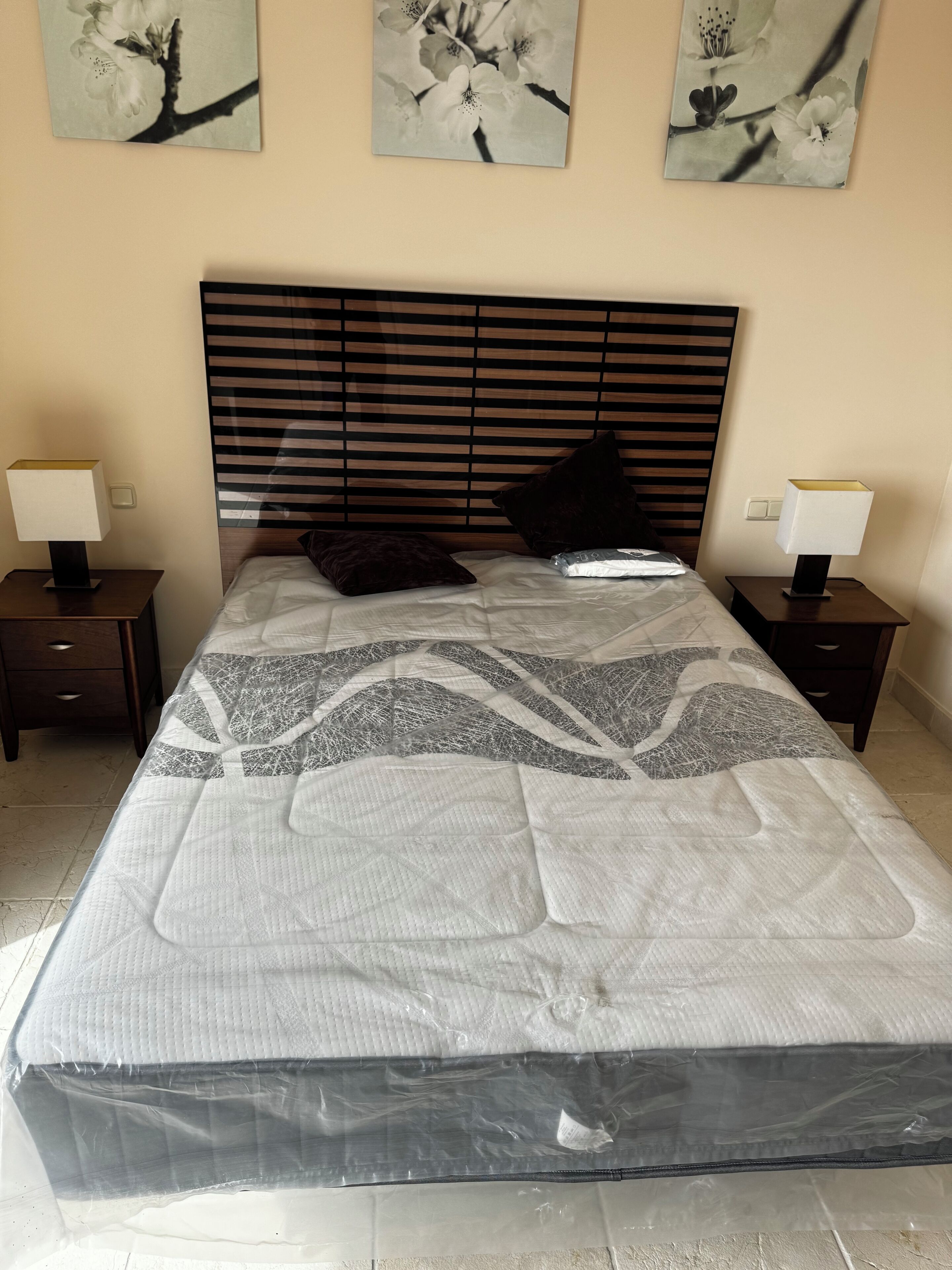 A neatly made bed with a patterned bedspread, two bedside tables with lamps, and three wall-mounted floral paintings.