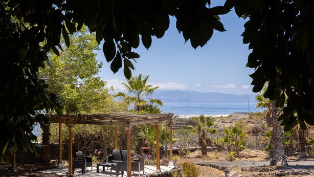 Un espacio de estar al aire libre cubierto con sillas y mesas, con vistas a la playa y montañas.