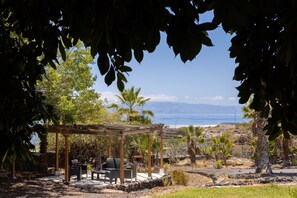 Un espacio de estar al aire libre cubierto con sillas y mesas, con vistas a la playa y montañas.