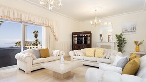 Un salón amplio con dos sofás blancos, una mesa de centro y un gran ventanal con cortinas.