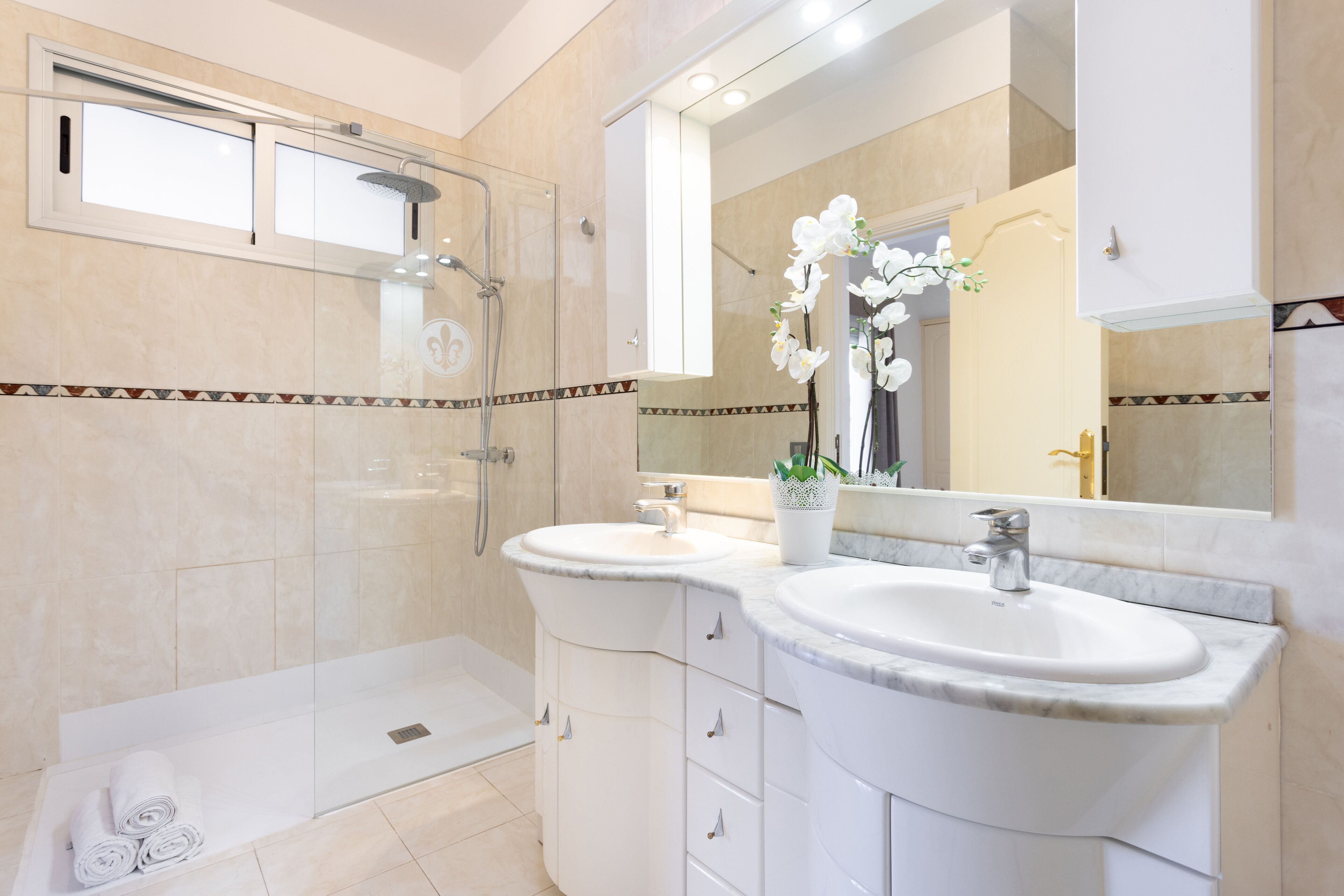 Une salle de bain moderne dotée d’une douche à parois de verre, de deux lavabos et d’un grand miroir.