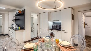Una cocina moderna con armarios blancos, un microondas y un comedor con mesa y sillas de vidrio.