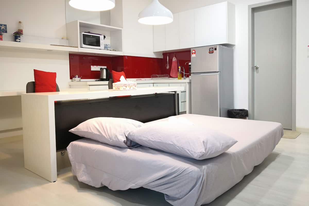 A compact bedroom with a bed, a small kitchenette, and a door.