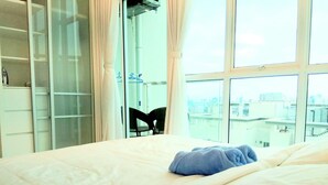 Ein Hotelzimmer mit Bett, Stuhl und Blick auf die Stadt durch große Fenster.