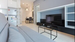 Ein modernes Wohnzimmer mit grauem Sofa, einem an einer schwarzen Wandeinheit montierten Flachbildfernseher und einem Essbereich mit Tisch und Stühlen.