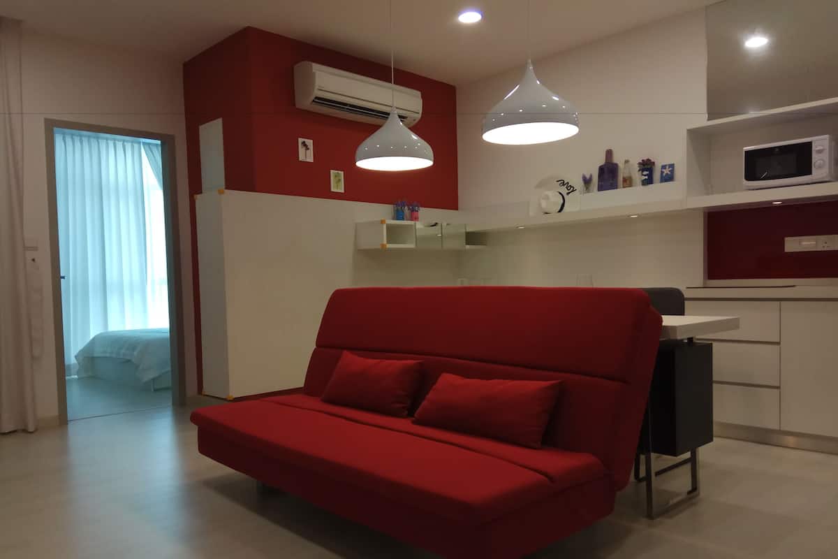 A modern room with a red sofa, a kitchen area with a microwave, and a large window with sheer curtains.