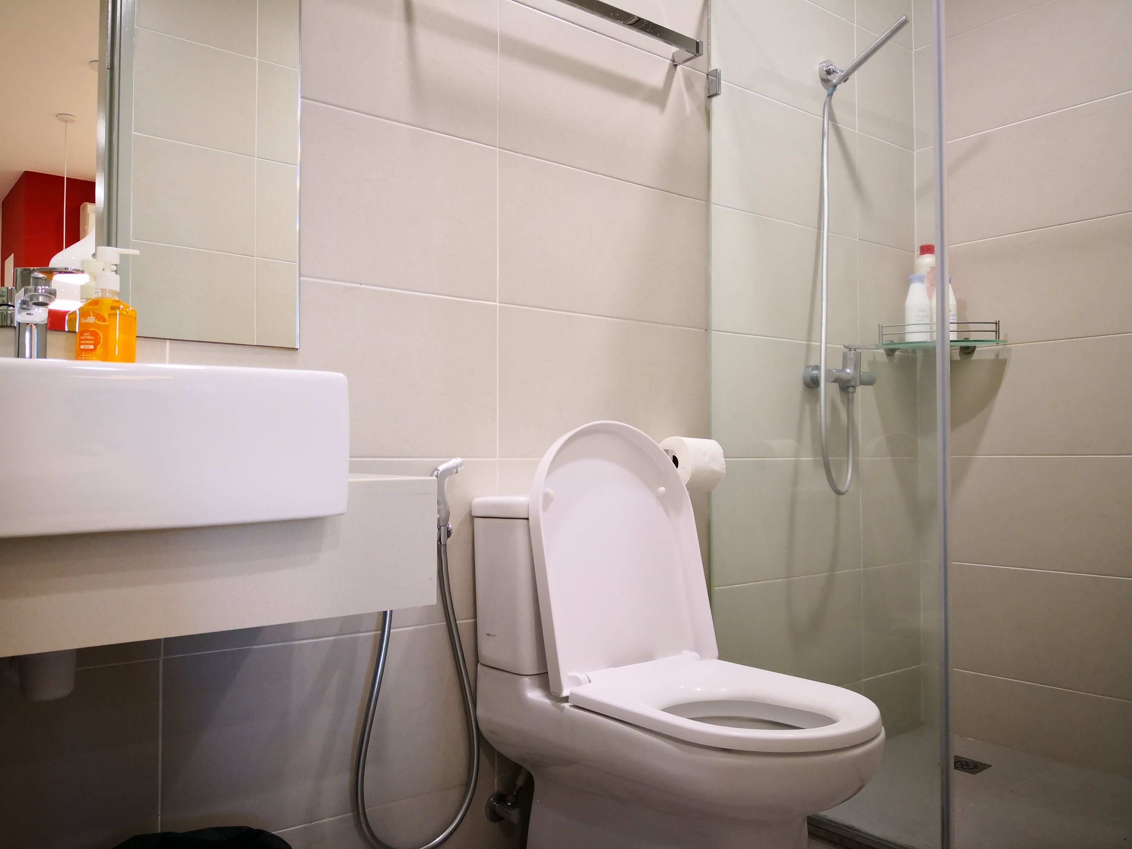 A modern bathroom with a toilet, a glass shower enclosure, and a sink with toiletries.