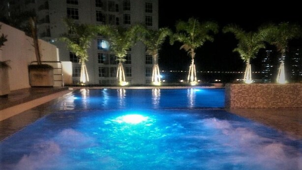 Ein beleuchteter Pool bei Nacht, mit Palmen und einem Gebäude im Hintergrund.