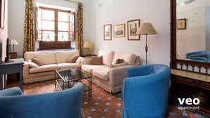 A living room with a sofa, armchairs, a coffee table, and a floor lamp. There are curtains, a mirror, and framed pictures on the wall. - 4 bedrooms, free parking. Santa Cruz quarter (Sevilla)