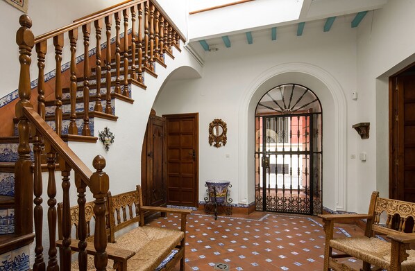 A spacious interior with a wooden staircase, a tiled floor, and a large arched doorway.