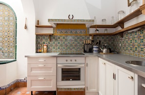 Una cucina compatta con mobili bianchi, forno integrato e zoccolo in piastrelle.
