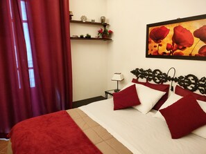 A hotel room with a large bed, red curtains, a bedside table with a lamp, and a wall-mounted shelf with decorative items. - Small jewel in the historic center of Catania (Catania)