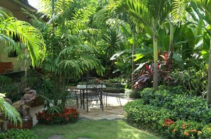 Un exuberante jardín con un patio de piedra, una mesa y sillas.