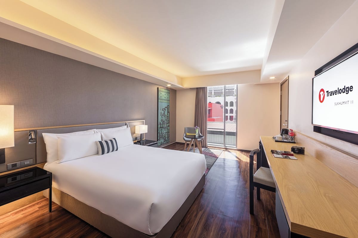 A modern hotel room with a large bed, a desk, and a balcony with a view.