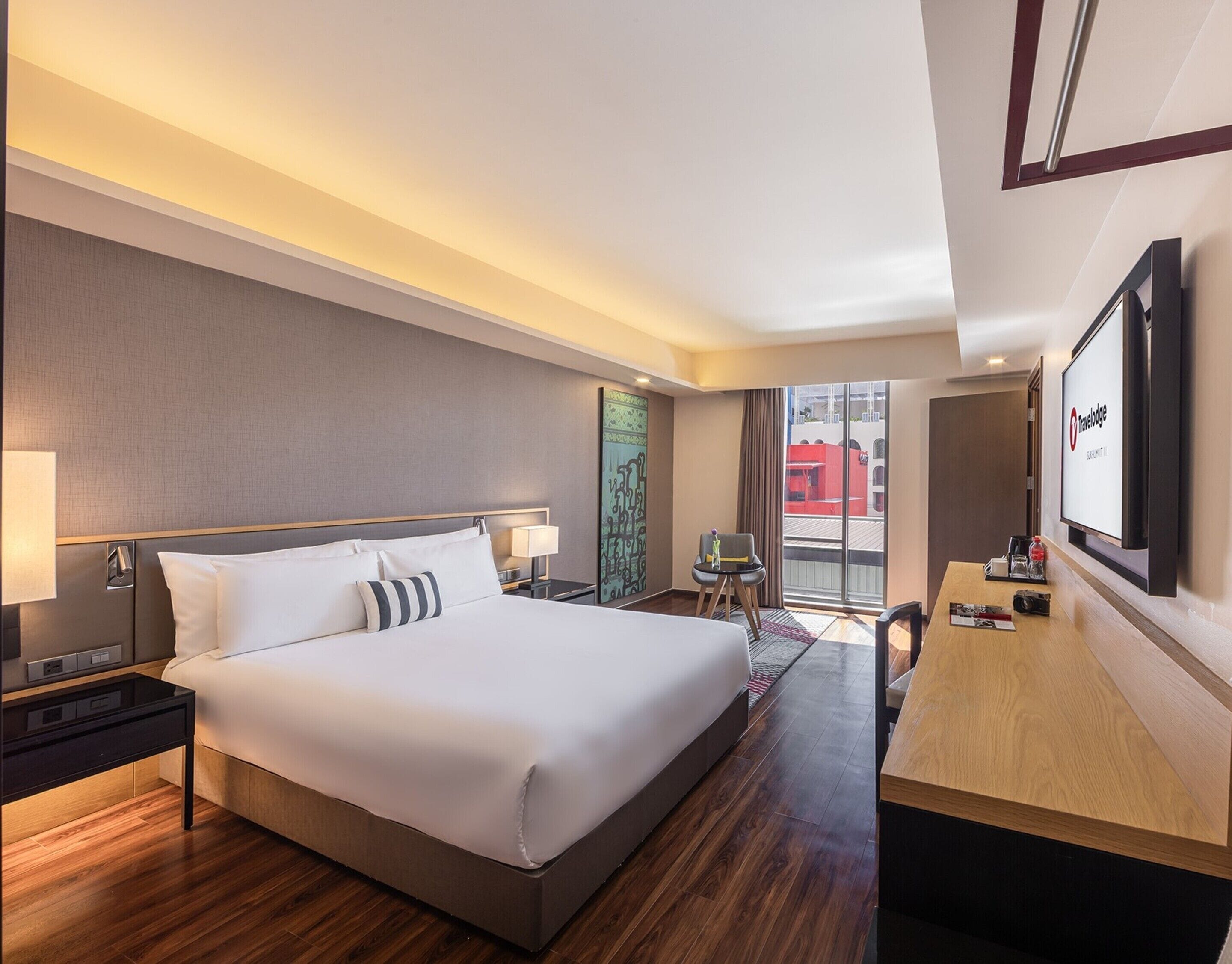 Una habitación de hotel moderna con una cama grande, mesitas de noche, un escritorio y un televisor.