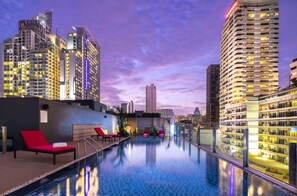 A rooftop infinity pool with red lounge chairs, surrounded by high-rise buildings and a city skyline at dusk. - Travelodge Sukhumvit 11 (Bangkok)
