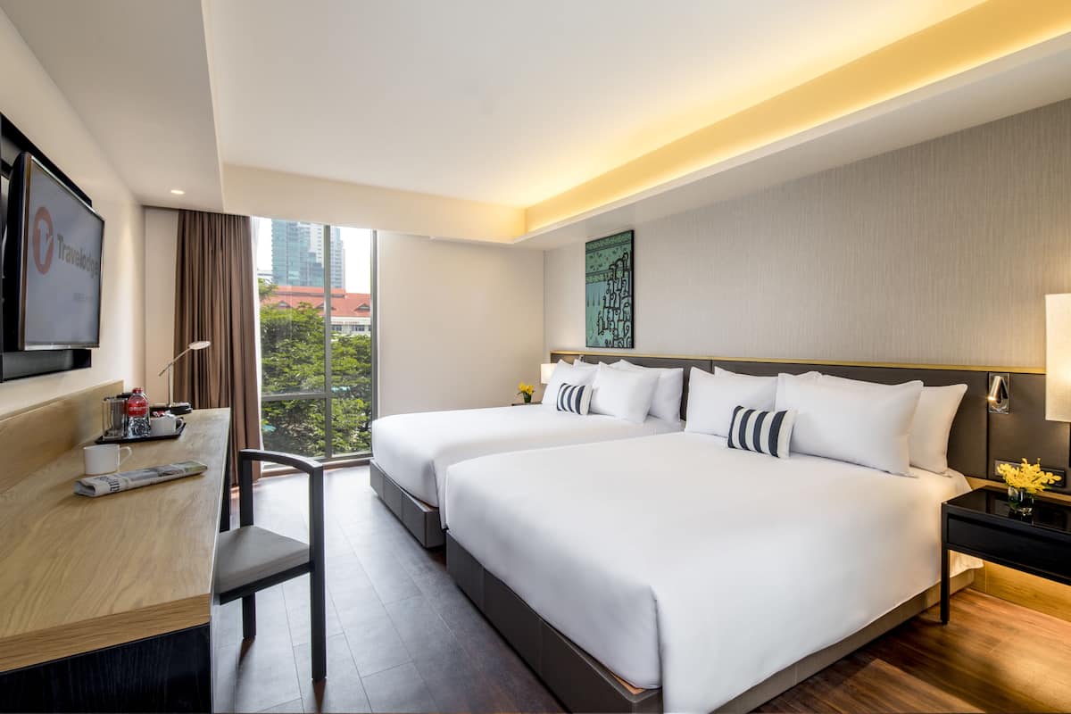 A hotel room with two beds, a desk, a TV, and a large window with a city view.