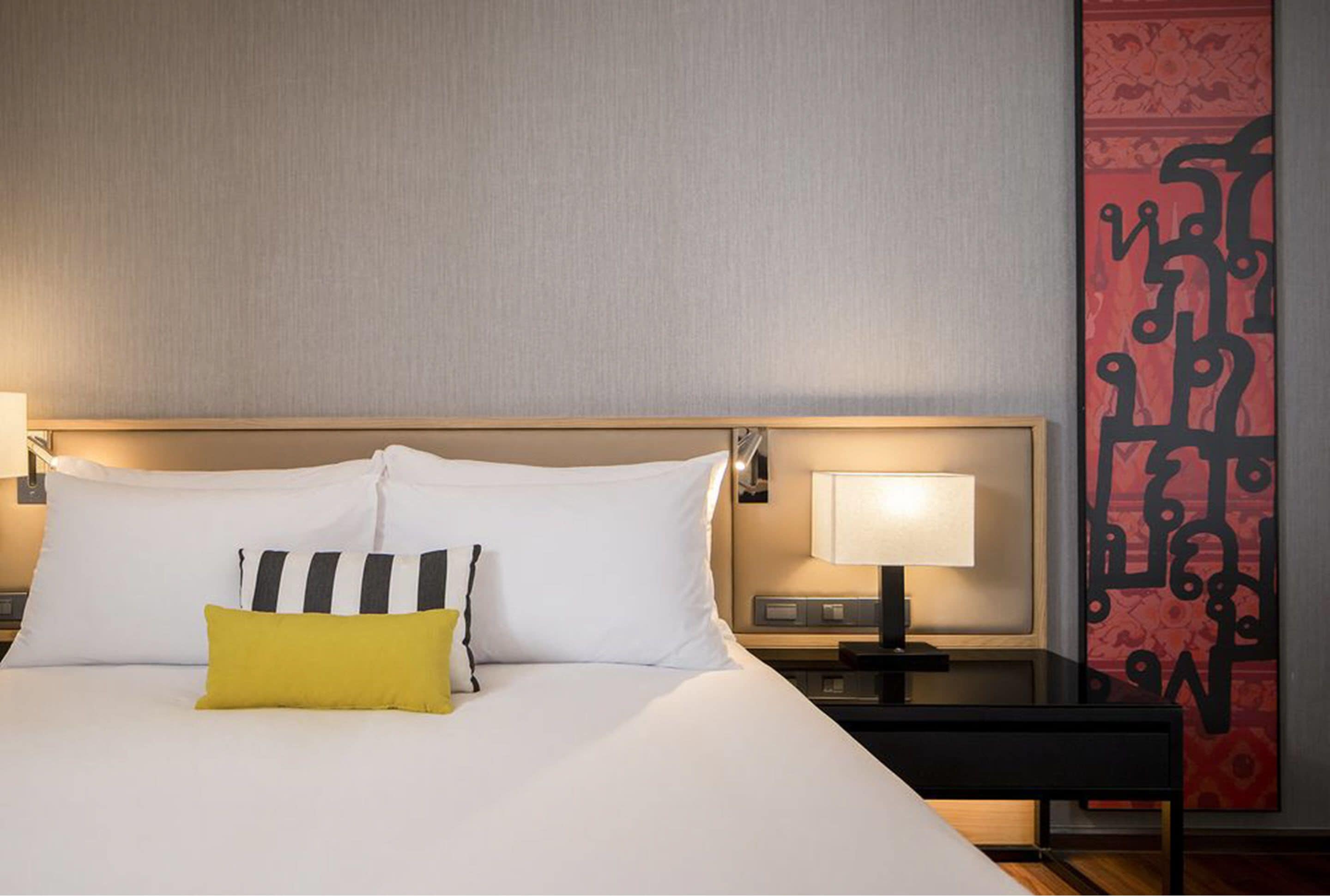 Una habitación de hotel con una cama grande, dos lámparas de noche, una mesita de noche y un adorno en la pared.