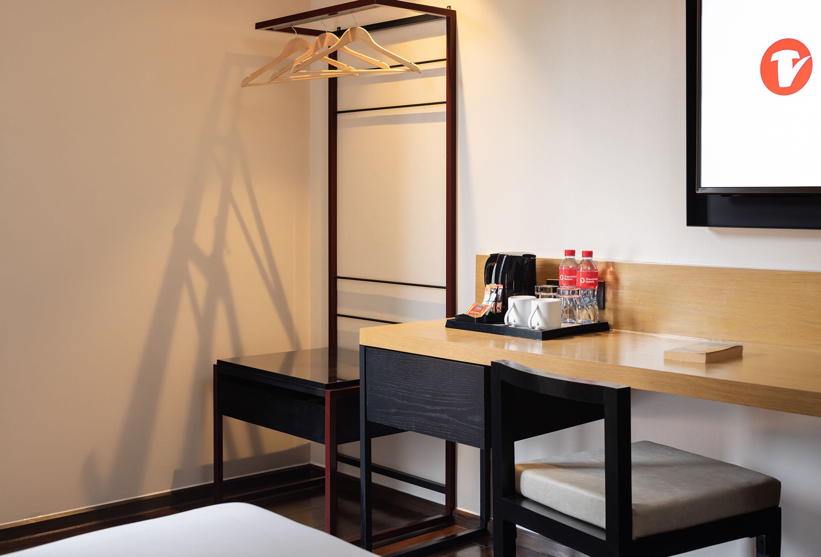 A hotel room with a wooden desk, two chairs, a hanging clothes rack, and a bed.