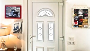 Una porta bianca con un pannello di vetro decorativo, una foto incorniciata di una nave, una bacheca con il menù a parete e una lampada su un tavolo.