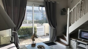 Una habitación con un ventanal, vistas a una casa, una escalera y un televisor sobre una repisa de madera.