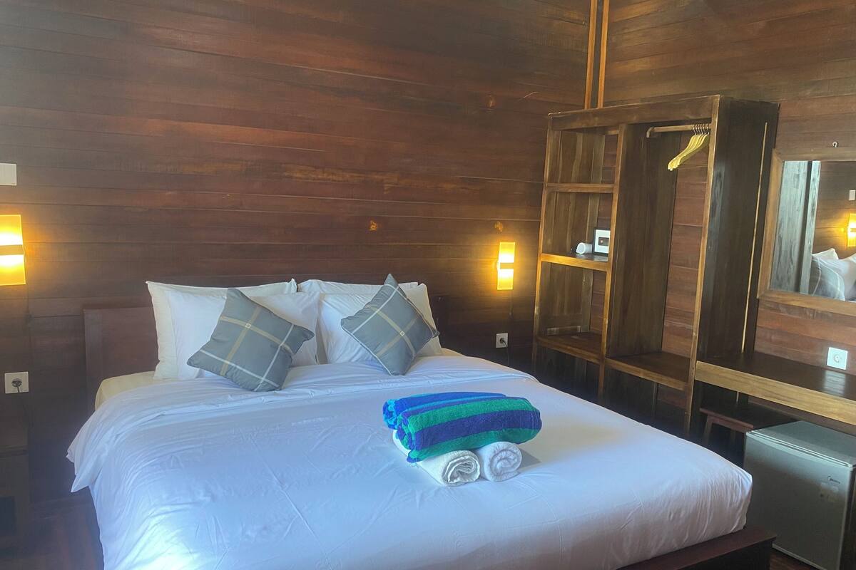 Un lit bien fait, avec des oreillers, une table de chevet, un miroir et une armoire, dans une pièce en bois.