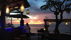 A seaside bar with hanging lights and a view of the sunset over the ocean. - Linda Beach Hotel (Lembongan Island)