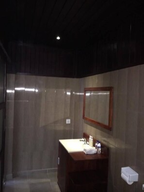 A bathroom with a wooden vanity, a mirror, and a towel dispenser. - Linda Beach Hotel (Lembongan Island)