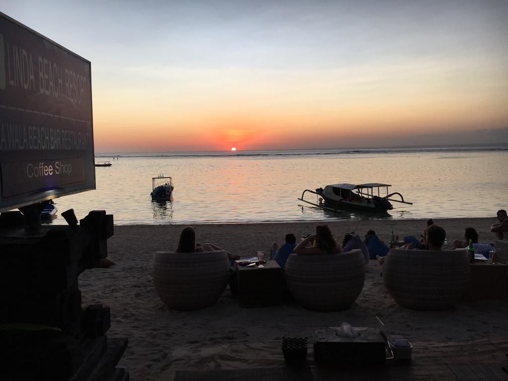 Une plage au coucher du soleil, avec un bateau et des gens qui se détendent sur le sable.