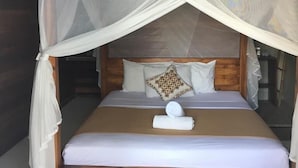 A bed with a canopy, a pillow, and a towel on the bed. - Linda Beach Hotel (Lembongan Island)