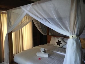 A hotel room with a canopy bed, a neatly made bed with a rolled towel and a flower, and a star-shaped pillow. - Linda Beach Hotel (Lembongan Island)