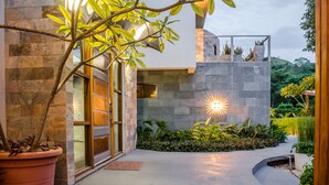 Un edificio moderno con fachada de piedra, entrada de vidrio y un jardín ajardinado con plantas en macetas y un sendero.