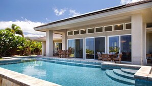 Ein Schwimmbad mit Terrassenbereich, inklusive Stühle und Tische, und ein Gebäude mit großen Fenstern.