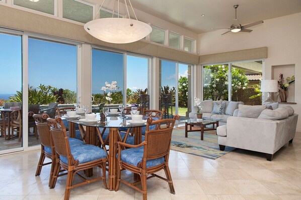 A spacious living area with a dining table, wicker chairs, a sofa, and a ceiling fan.