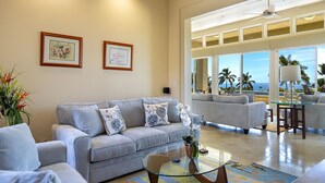 Ein geräumiges Wohnzimmer mit grauem Sofa, einem Glastisch und Meerblick durch große Fenster.