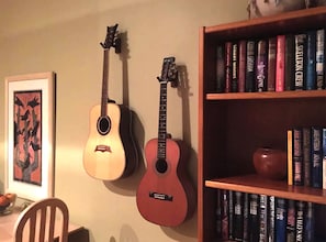 Music and literature come together in this cozy space, featuring a bookshelf, acoustic guitars, and a comfortable chair.