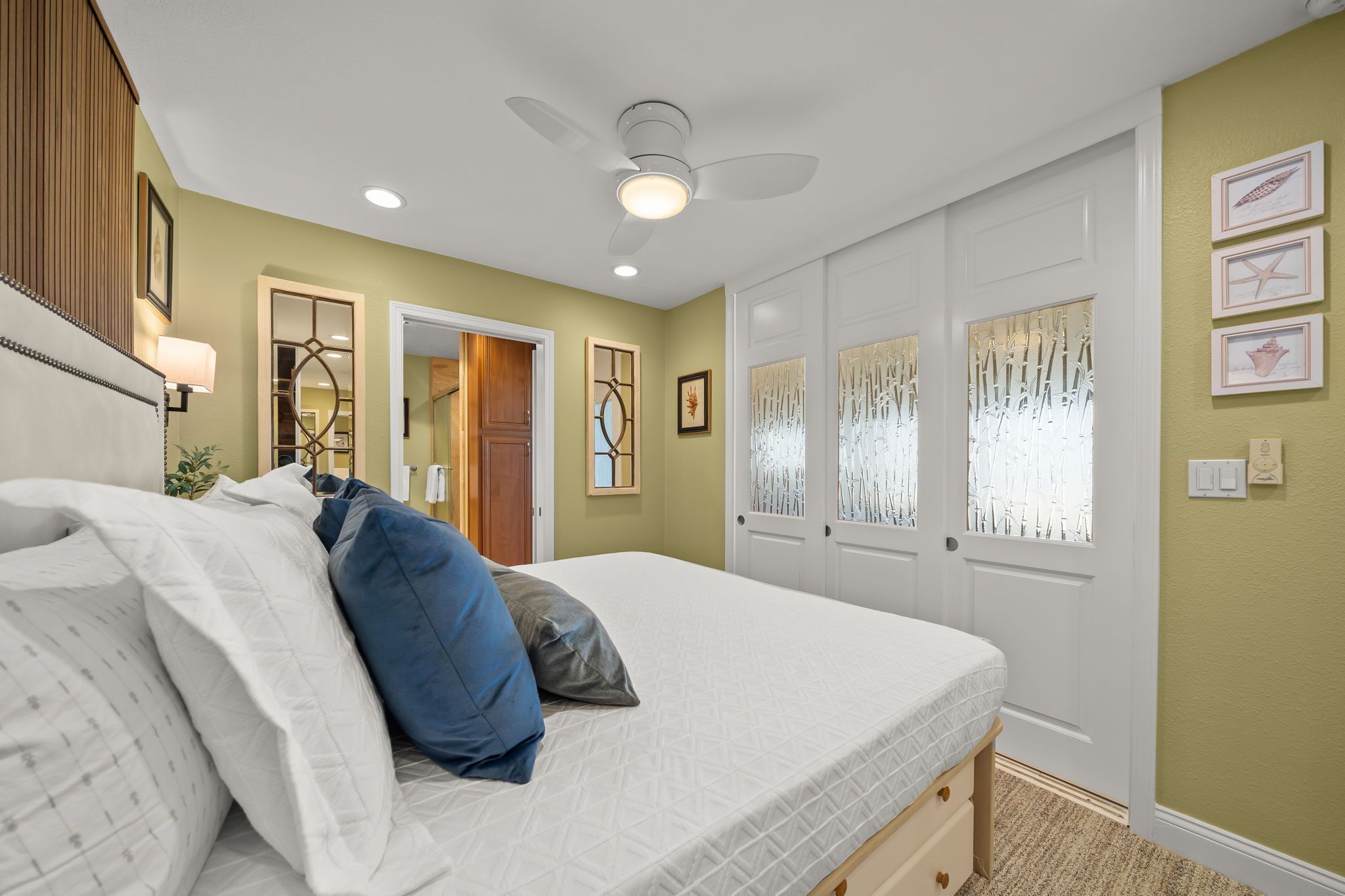 A bedroom with a bed, a ceiling fan, a door with frosted glass panels, and wall-mounted artwork.