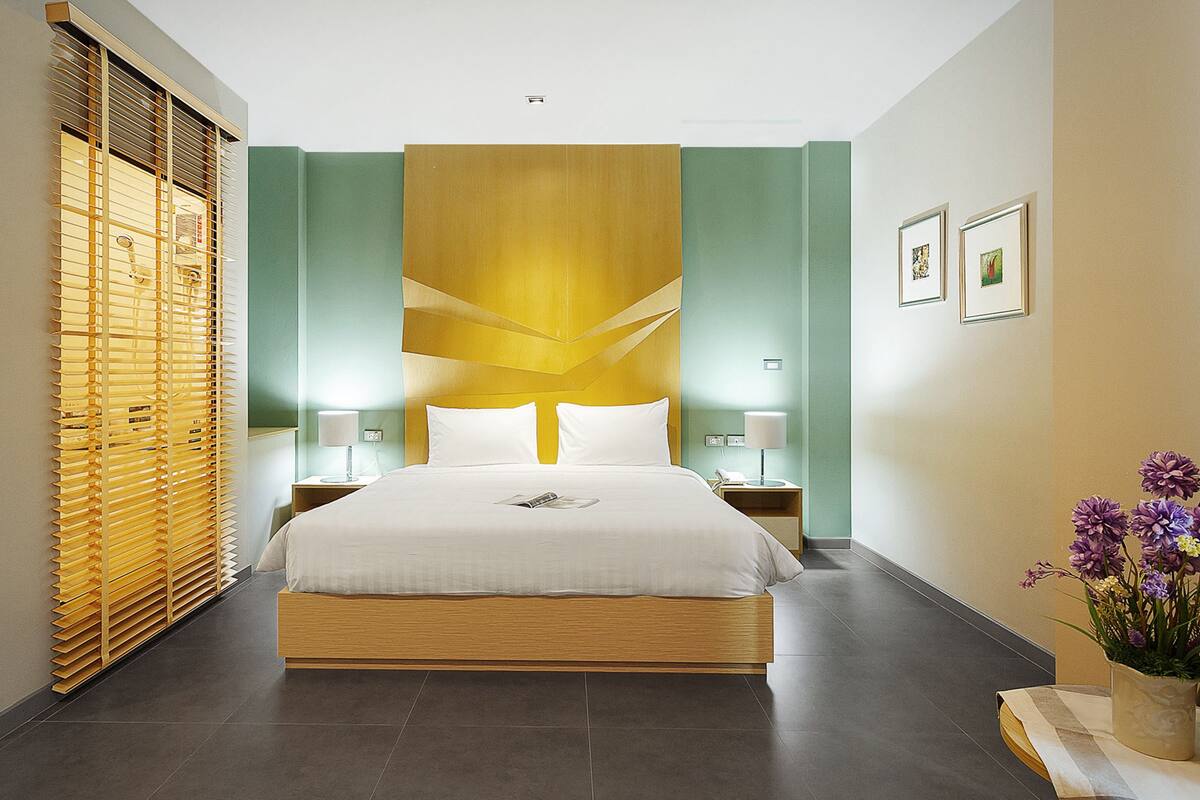 A modern hotel room with a large bed, wooden headboard, and a nightstand with a lamp.