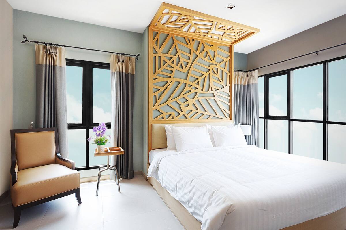 A hotel room with a large bed, a chair, a small table with a vase, and a decorative wooden partition.