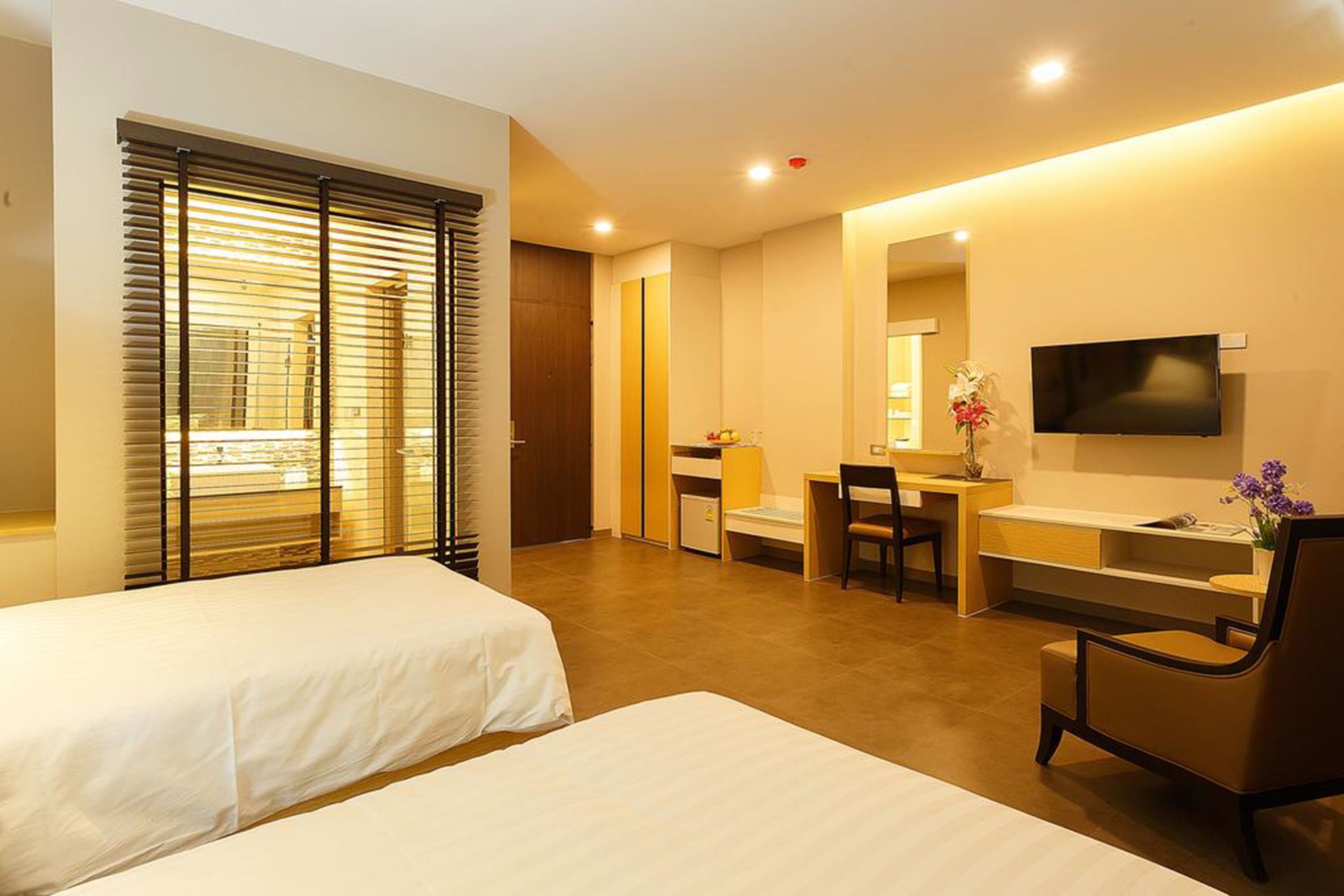 A hotel room with two beds, a desk, a chair, a TV, and a bathroom.