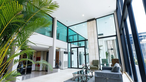 A spacious lobby with a modern design, featuring a glass wall, a seating area with a sofa and chairs, and a coffee table. - Green Point Residence Hotel (Bangkok)