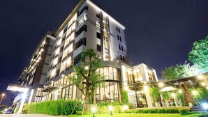 A modern multi-story hotel with a glass facade, outdoor seating area, and well-lit entrance. - Green Point Residence Hotel (Bangkok)