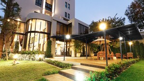 A hotel courtyard with outdoor seating, a dog, and a well-lit entrance. - Green Point Residence Hotel (Bangkok)