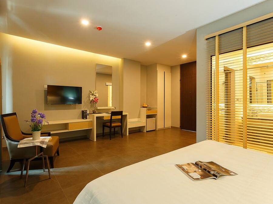 Una habitación de hotel moderna con cama, escritorio, silla, televisor y ventana con persianas.