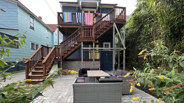 A two-story house with a wooden staircase, outdoor seating area, and laundry hanging on the balcony. - Cozy Downtown Condo(Dog Friendly) 3.5 Blocks to Beach.1 block to Washington Mall (Cape May)