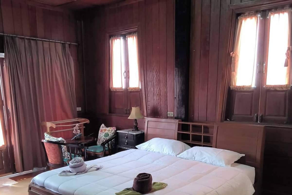 Une pièce en bois avec un grand lit, une table de chevet, une chaise et une fenêtre avec des rideaux.