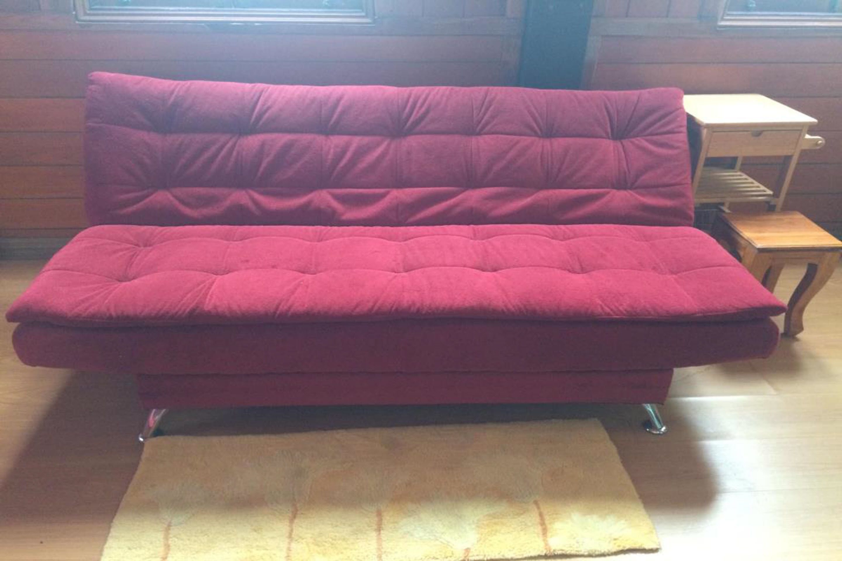 A red sofa with a tufted backrest and metal legs, placed on a wooden floor with a beige rug.